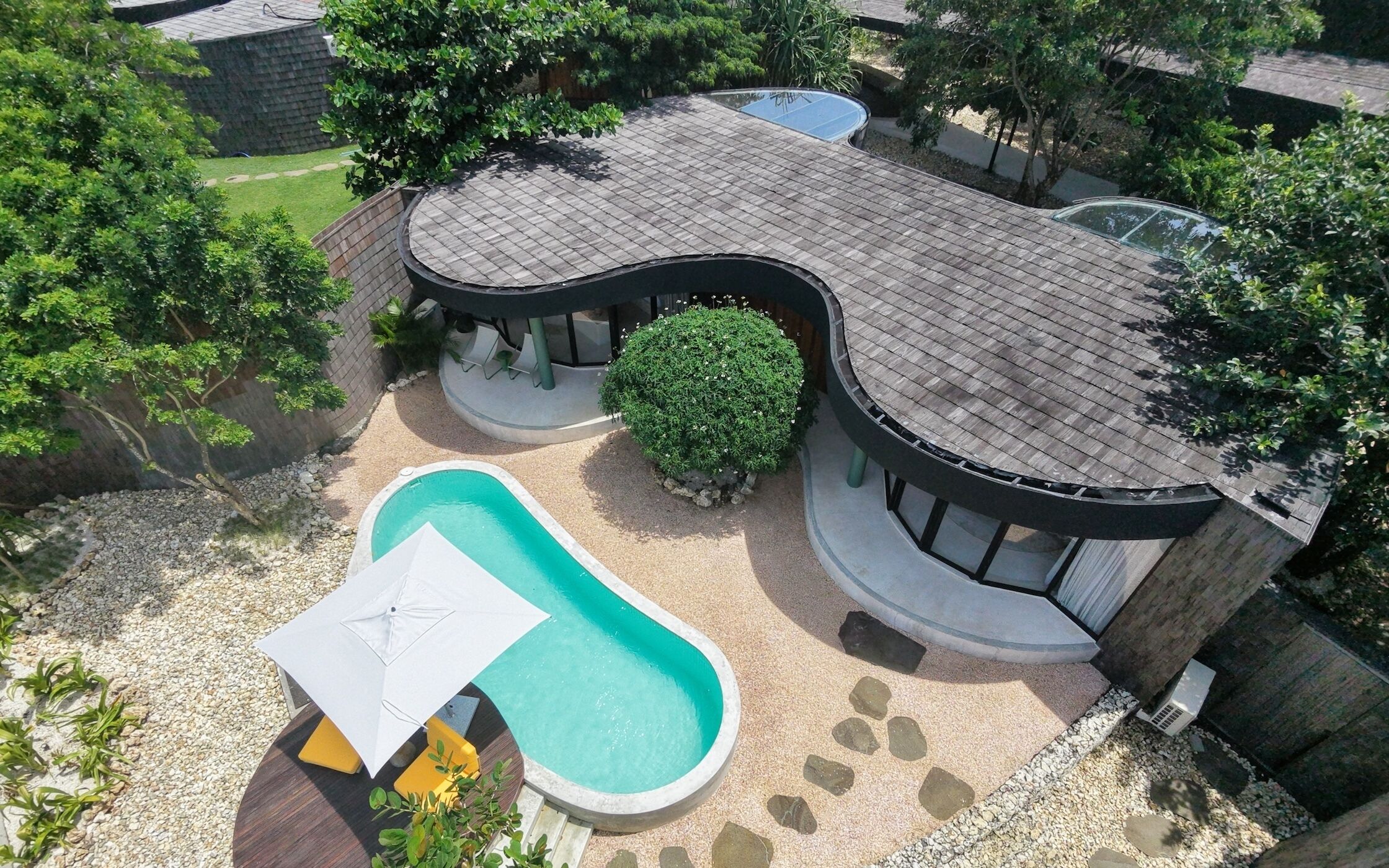 A house with a curved roof, a swimming pool, and a garden area.