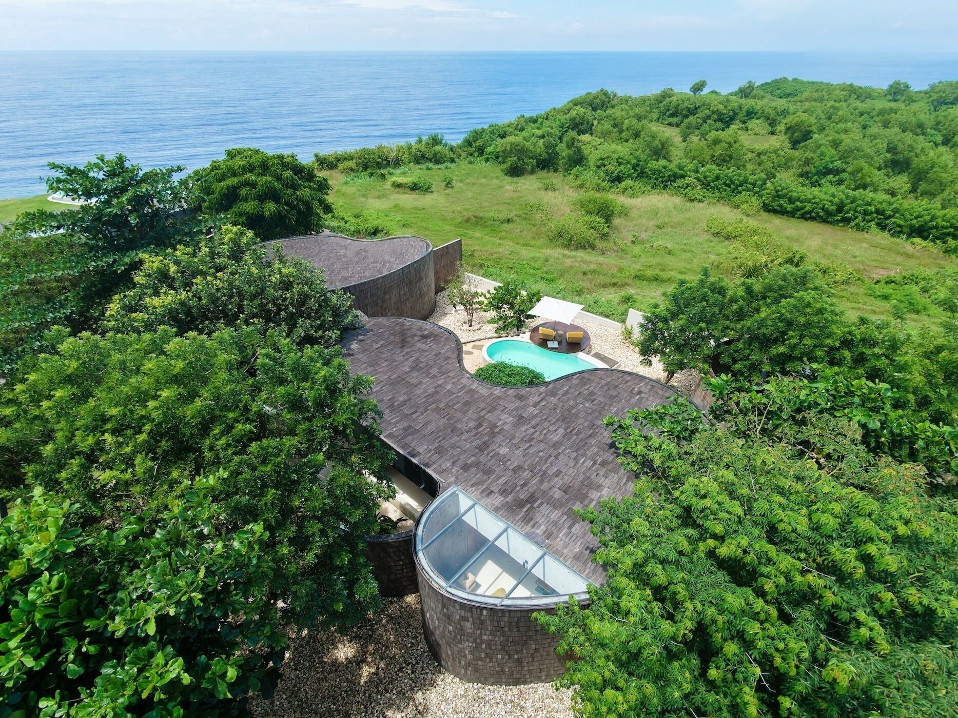 A house with a swimming pool surrounded by lush greenery and a view of the ocean.