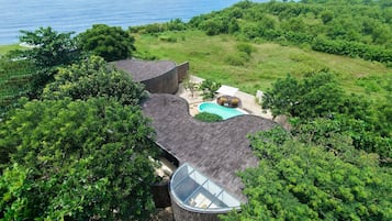 A house with a swimming pool surrounded by lush greenery and a view of the ocean.