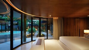 A modern interior with a curved ceiling, a large bed, and a view of a swimming pool and garden. - Nya Uluwatu (Pecatu)