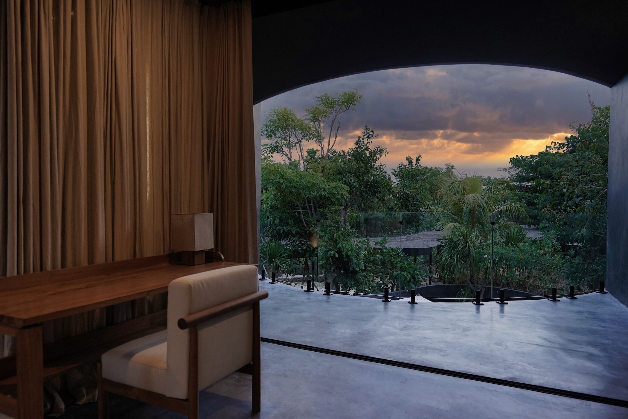 A room with a view of a garden at sunset.