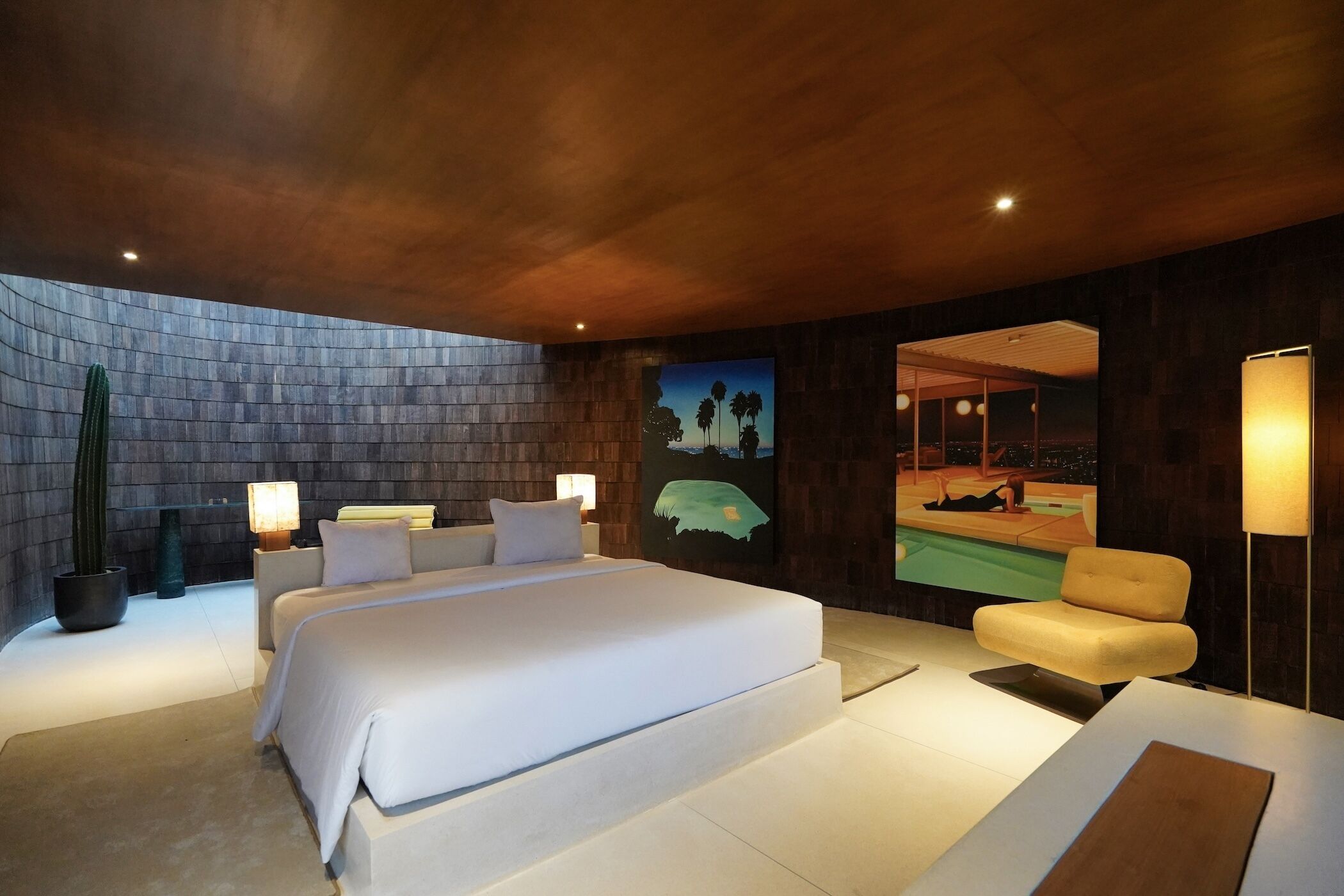 Une chambre moderne avec un grand lit, un canapé, un téléviseur fixé au mur et un cactus.
