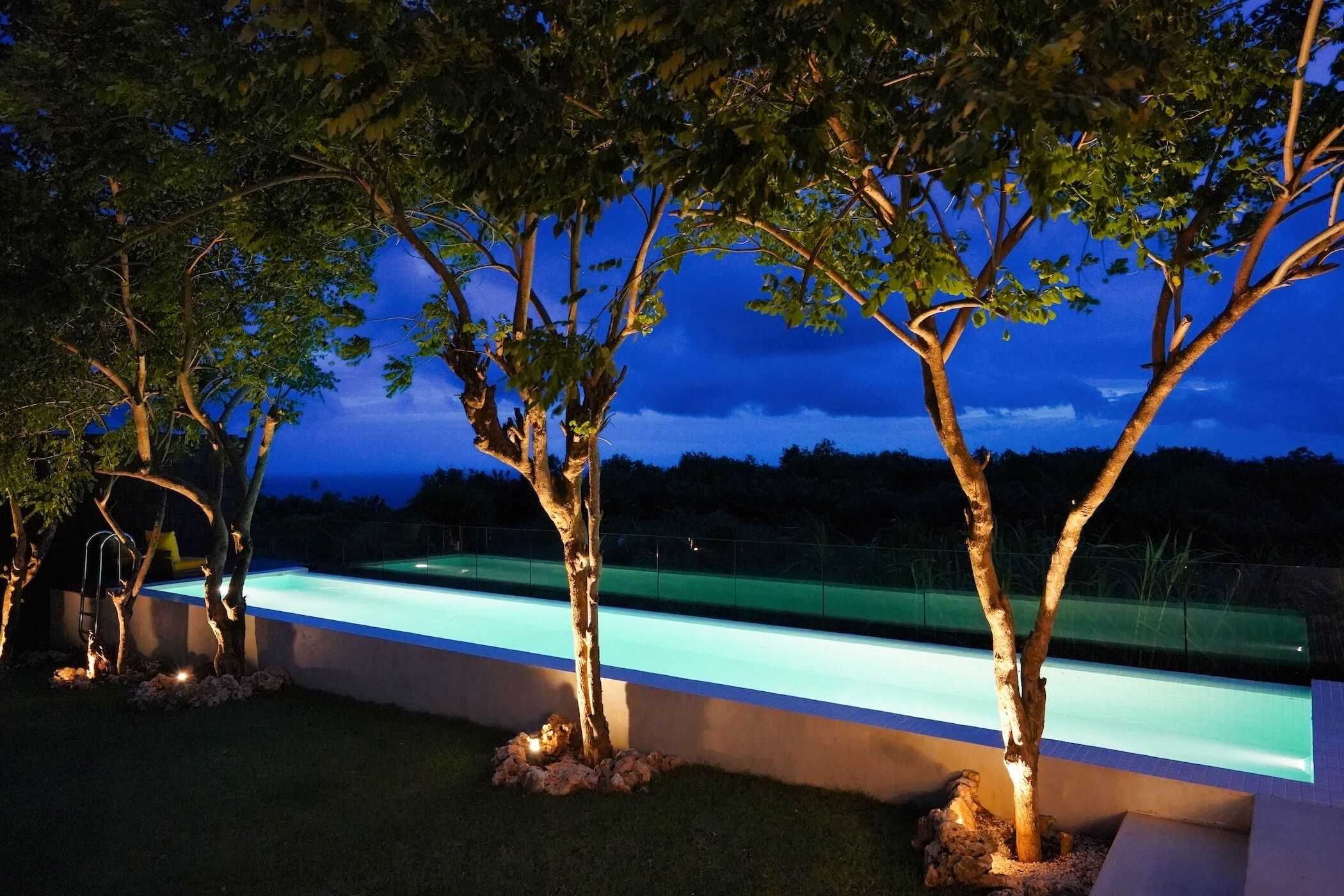 A swimming pool with a clear blue water feature, surrounded by trees and a low wall.
