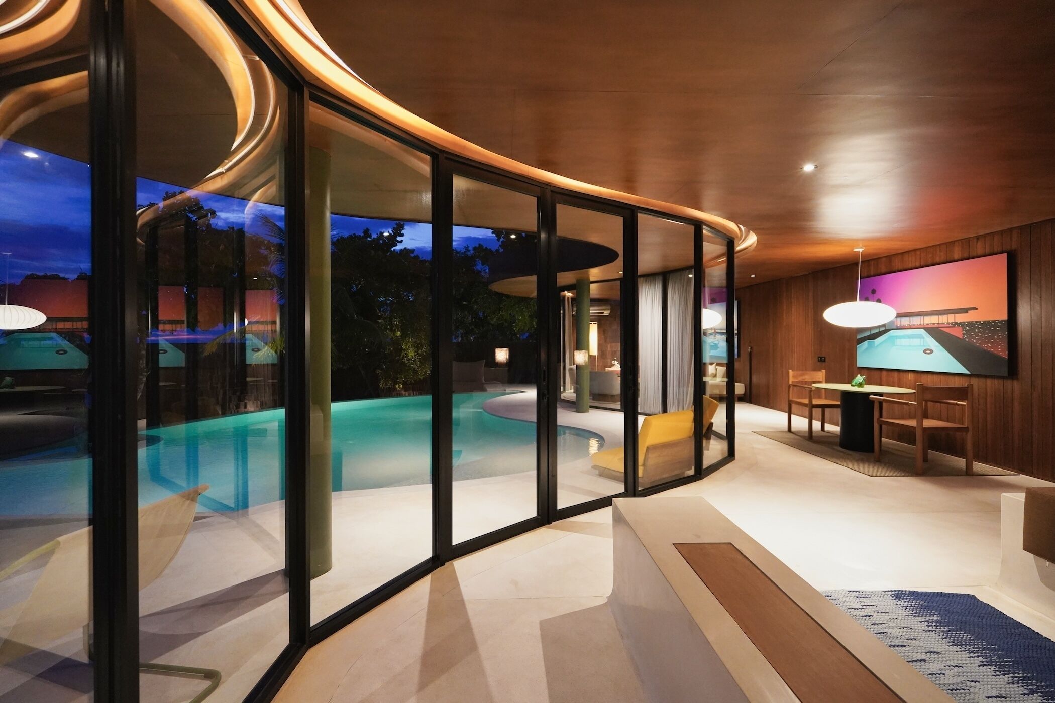 A modern interior with a glass-enclosed pool area, a dining area with a table and chairs, and a large painting on the wall.