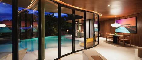 A modern interior with a glass-enclosed pool area, a dining area with a table and chairs, and a large painting on the wall.