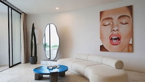 A modern living room with a round coffee table, a sofa, a cactus, and a large abstract painting on the wall. - Nya Uluwatu (Pecatu)