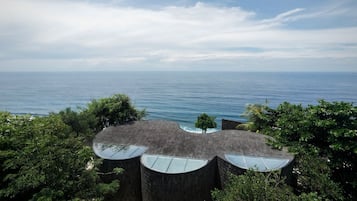 Un edificio moderno con un diseño de techo curvo único, rodeado de exuberante vegetación y vistas a un mar tranquilo.