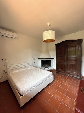 Un dormitorio con cama, un calentador en la pared, una lámpara colgante y un armario de madera.