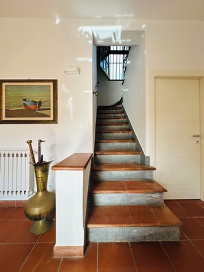 A staircase with a white door at the top, a radiator, and a framed painting on the wall. - Sant'Elme 87 (Forte dei Marmi)