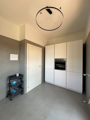 Una habitación con puerta blanca, armario blanco, horno empotrado y una lámpara en el techo.