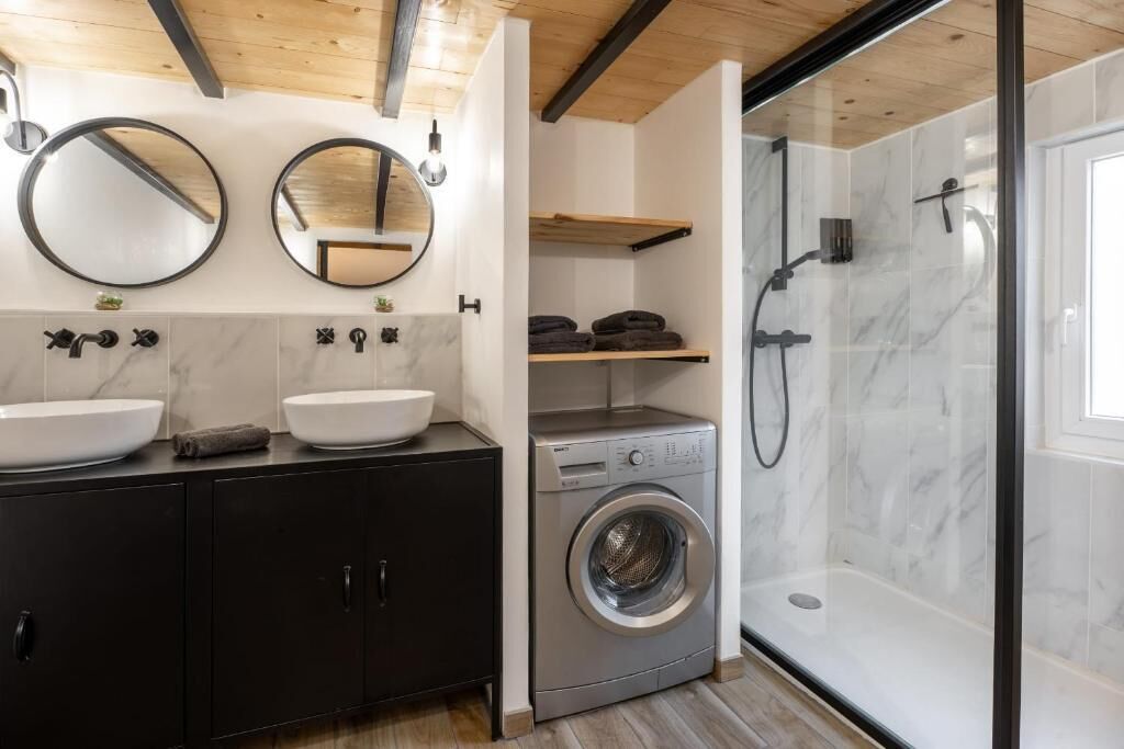 A modern bathroom with two sinks, a washing machine, and a glass-enclosed shower.