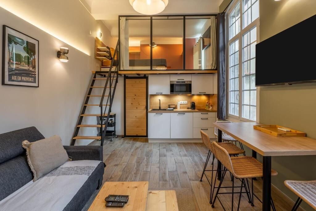 A compact living space with a loft bedroom, kitchenette, and a dining area with a wooden table and chairs.