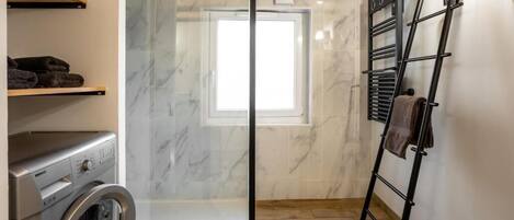 A laundry room with a washing machine, a glass shower enclosure, and a towel rack.