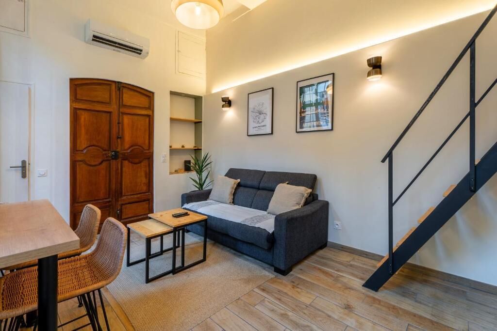 A living room with a sofa, a dining table, chairs, a staircase, and a wall-mounted air conditioner.