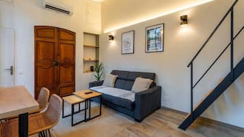 A living room with a sofa, a dining table, chairs, a staircase, and a wall-mounted air conditioner.