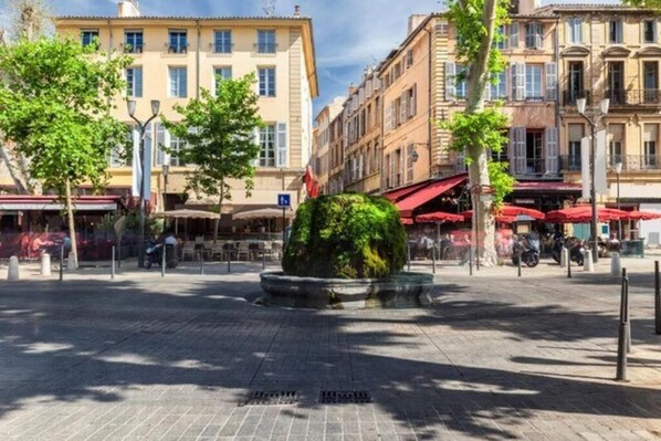 A paved square with a central round planter, surrounded by buildings with balconies and awnings, under a clear sky. - Duplex Mirabeau (Aix-en-Provence)