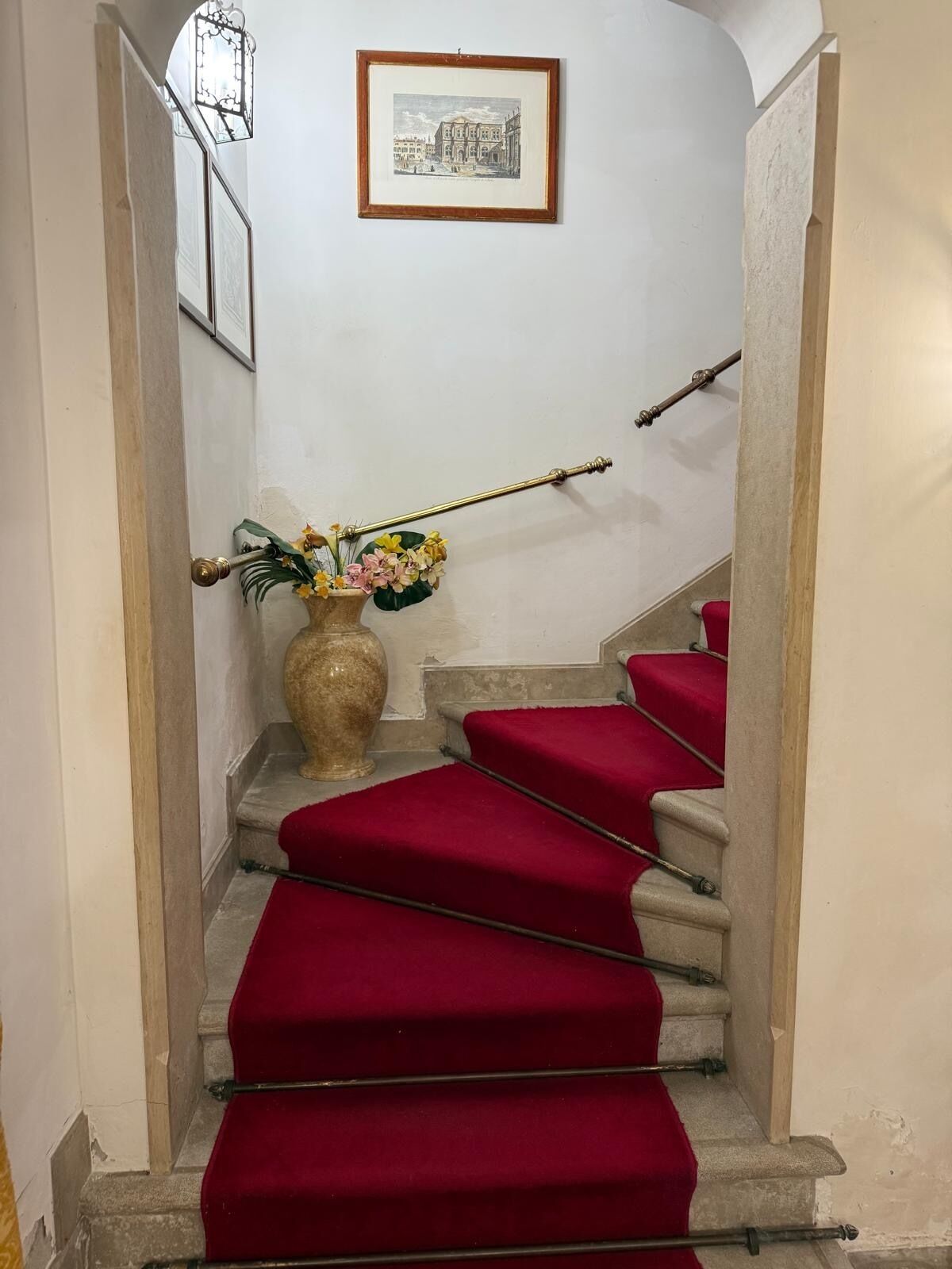 A staircase with red carpeted steps, a decorative vase with flowers, and a framed picture on the wall.