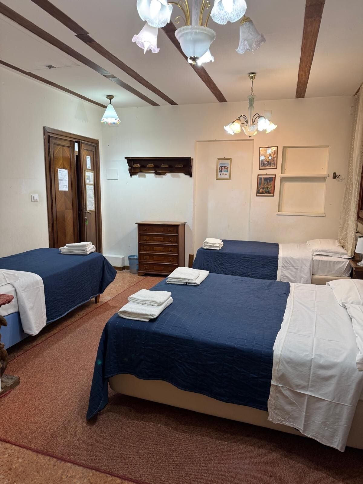 A hotel room with two beds, a wooden dresser, a desk, and a chandelier.
