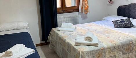 Une chambre avec deux lits, une fenêtre avec des rideaux, un radiateur et un petit tableau accroché au mur.