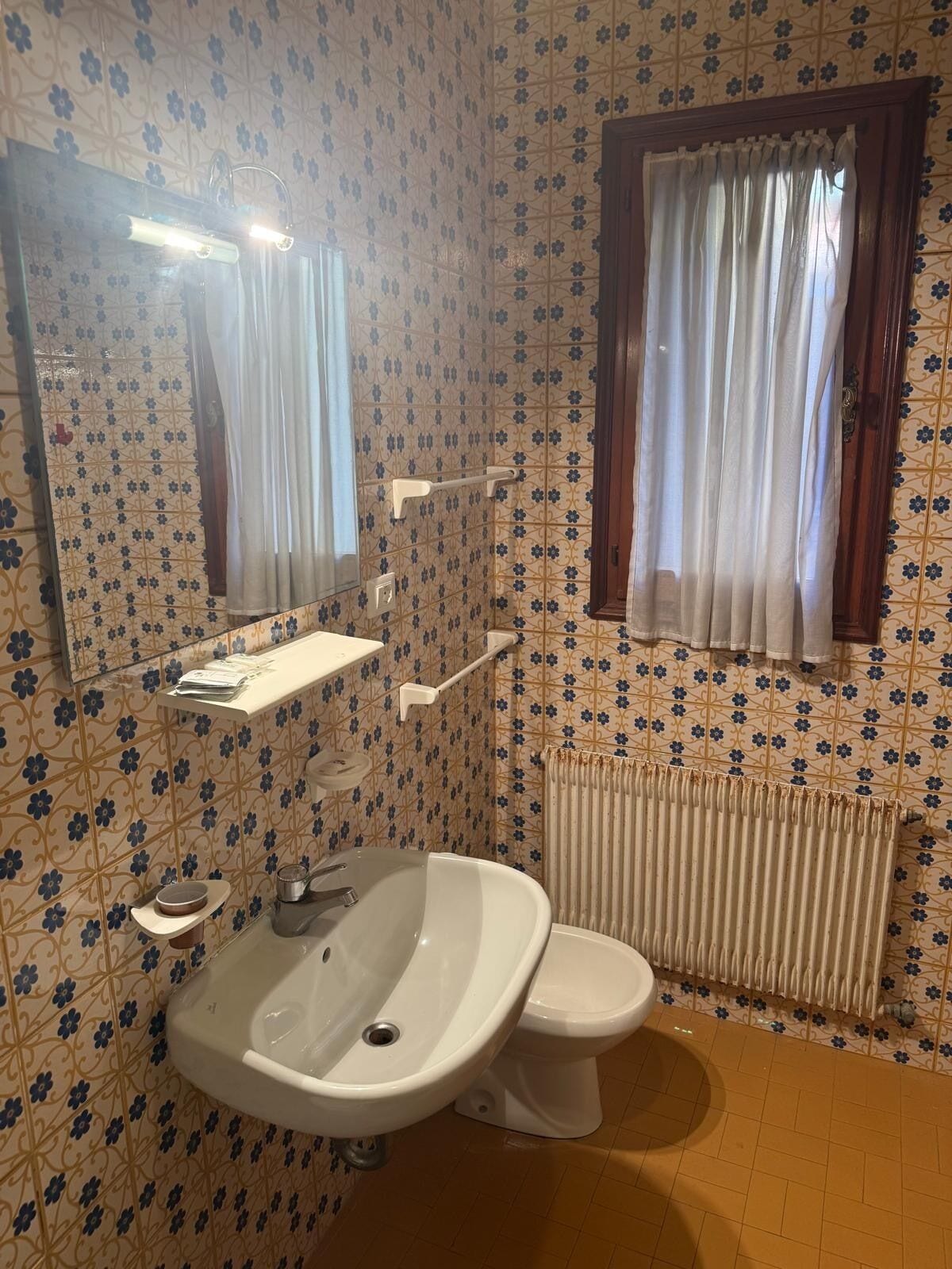 Ein Badezimmer mit Waschbecken, Toilette, Spiegel und einem fenster mit Vorhängen.