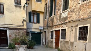A courtyard with stone paving, a potted plant, and a building with a sign. - ALLOGGI ALLA SCALA (Venice)