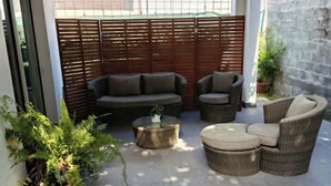 Een terras met een houten dak, een bank, twee fauteuils en een ronde salontafel.