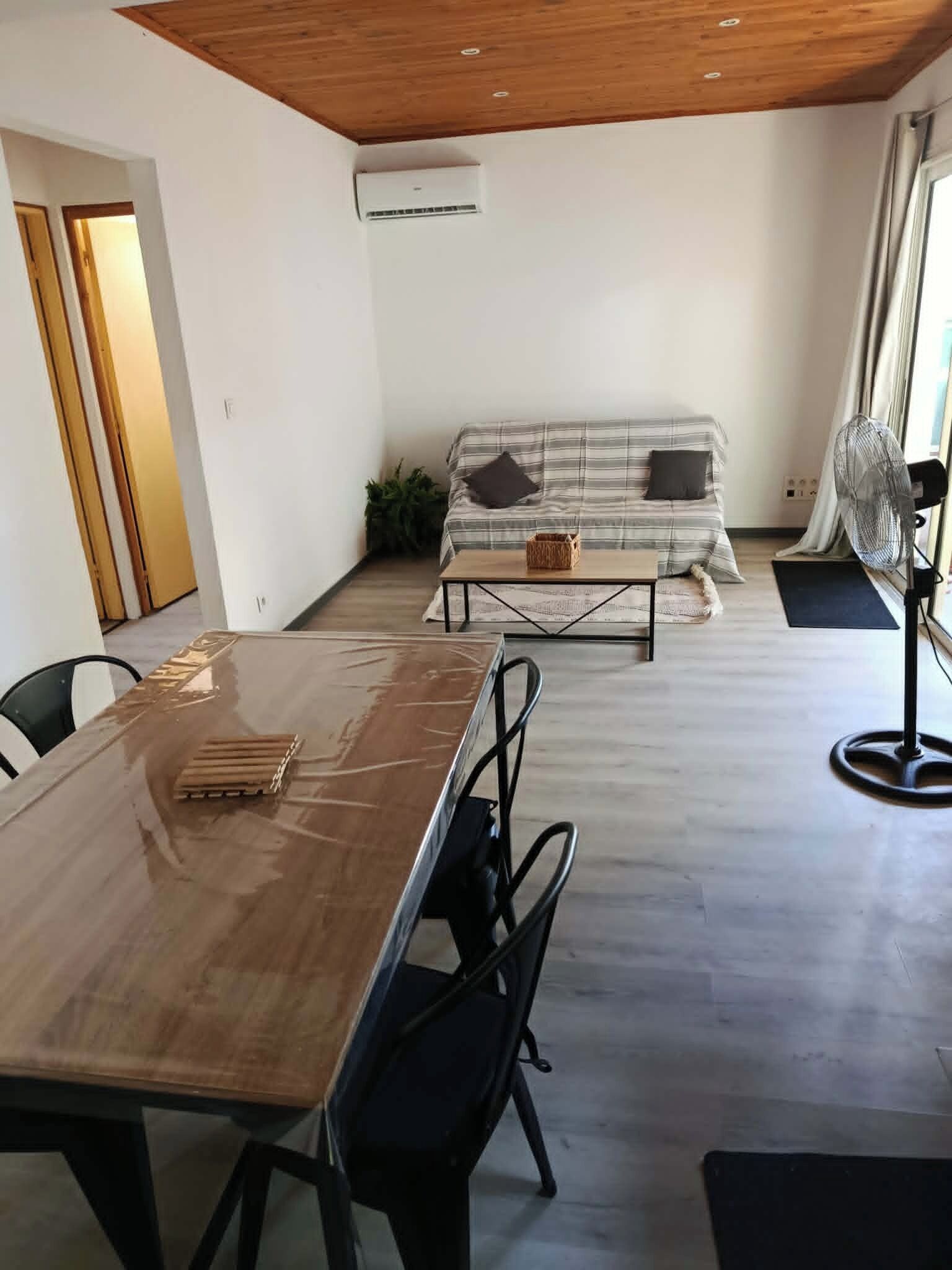 A modern living room with a wooden ceiling, a sofa, a coffee table, and a fan.