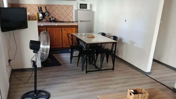 Een ruimtelijk ingerichte leefruimte met eethoek, kitchenette en een aan de muur bevestigde televisie.