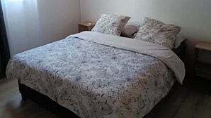 Een slaapkamer met een bed, beddengoed met bloemenprint, houten vloer en een houten plafond.