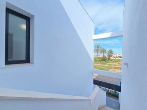 A white building with a window and a view of palm trees and buildings in the distance. - Kristal by Interhome (Mar de Cristal/Playa Honda)