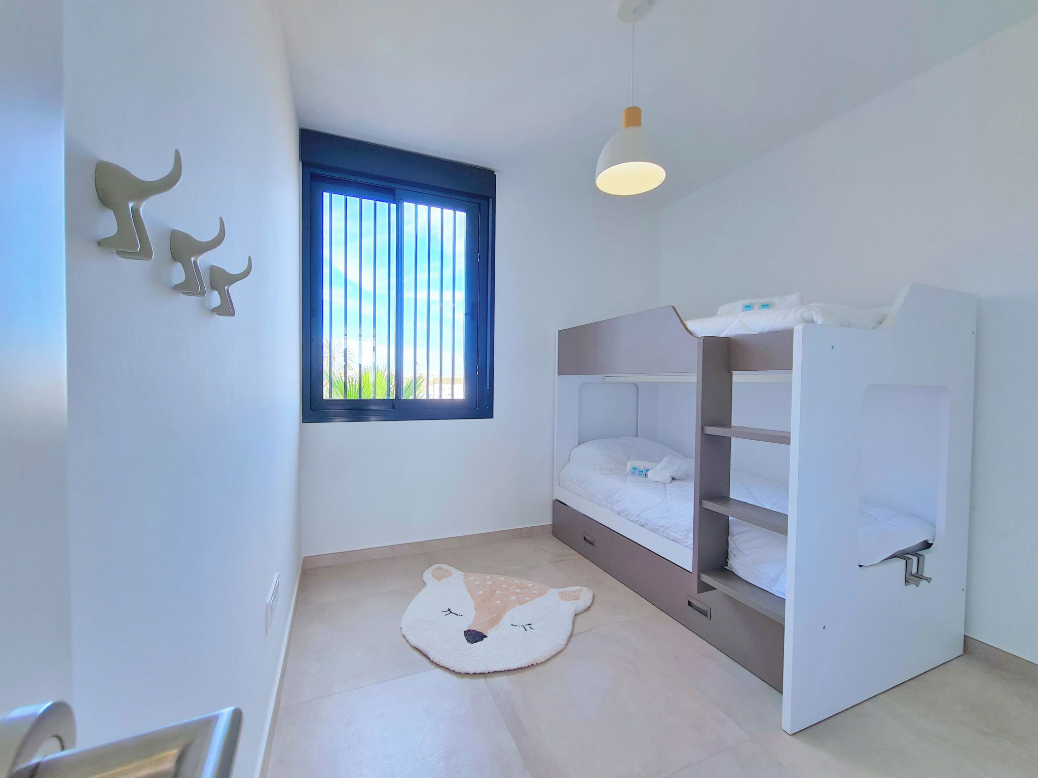 A child's bedroom with bunk beds, a window with bars, a ceiling light, and a bear-themed rug.
