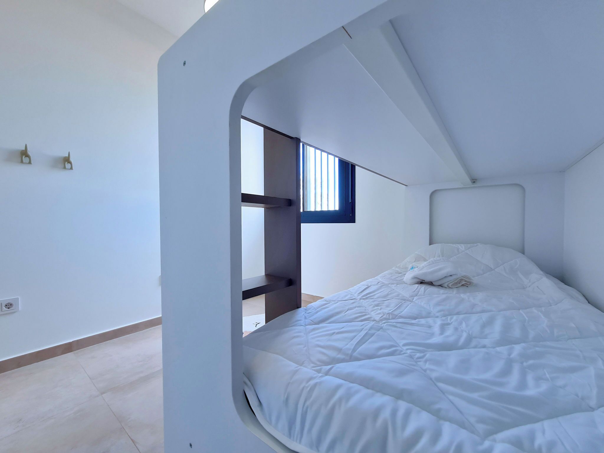 A bunk bed with a window, white walls, and a simple design.