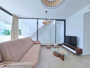 A modern living room with a sofa, a glass coffee table, a TV, and a staircase leading to an upper floor. - Kristal by Interhome (Mar de Cristal/Playa Honda)