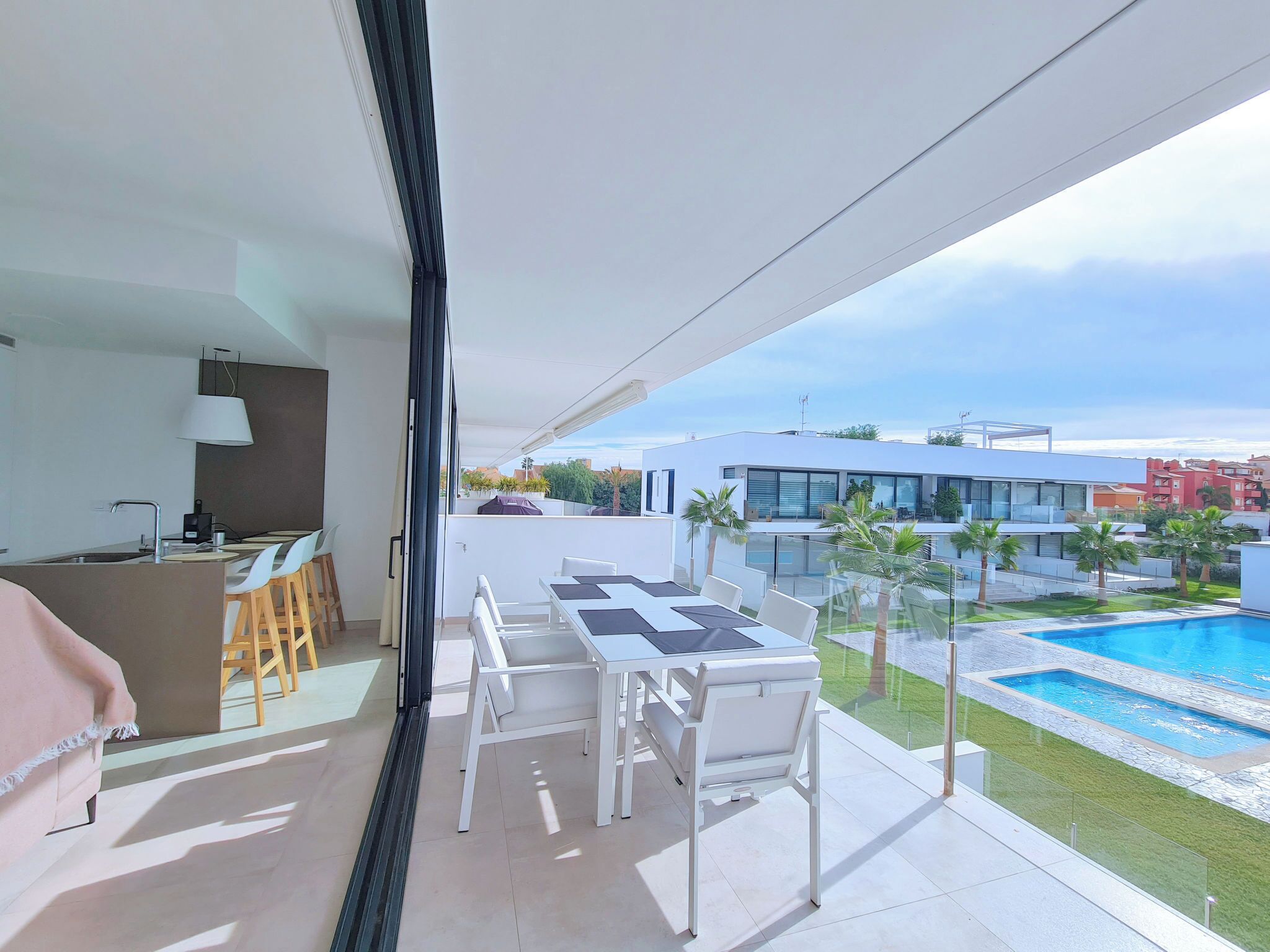 Un balcon doté d’un espace repas, d’une cuisine et offrant une vue sur une piscine et des bâtiments modernes.