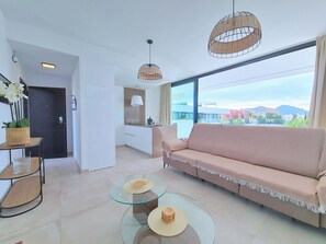 A modern living room with a sofa, two glass tables, and a view of the cityscape through large windows. - Kristal by Interhome (Mar de Cristal/Playa Honda)