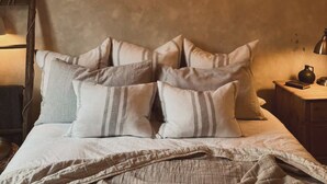 Een bed met meerdere kussens en een nachtkastje met een lamp en een boek.