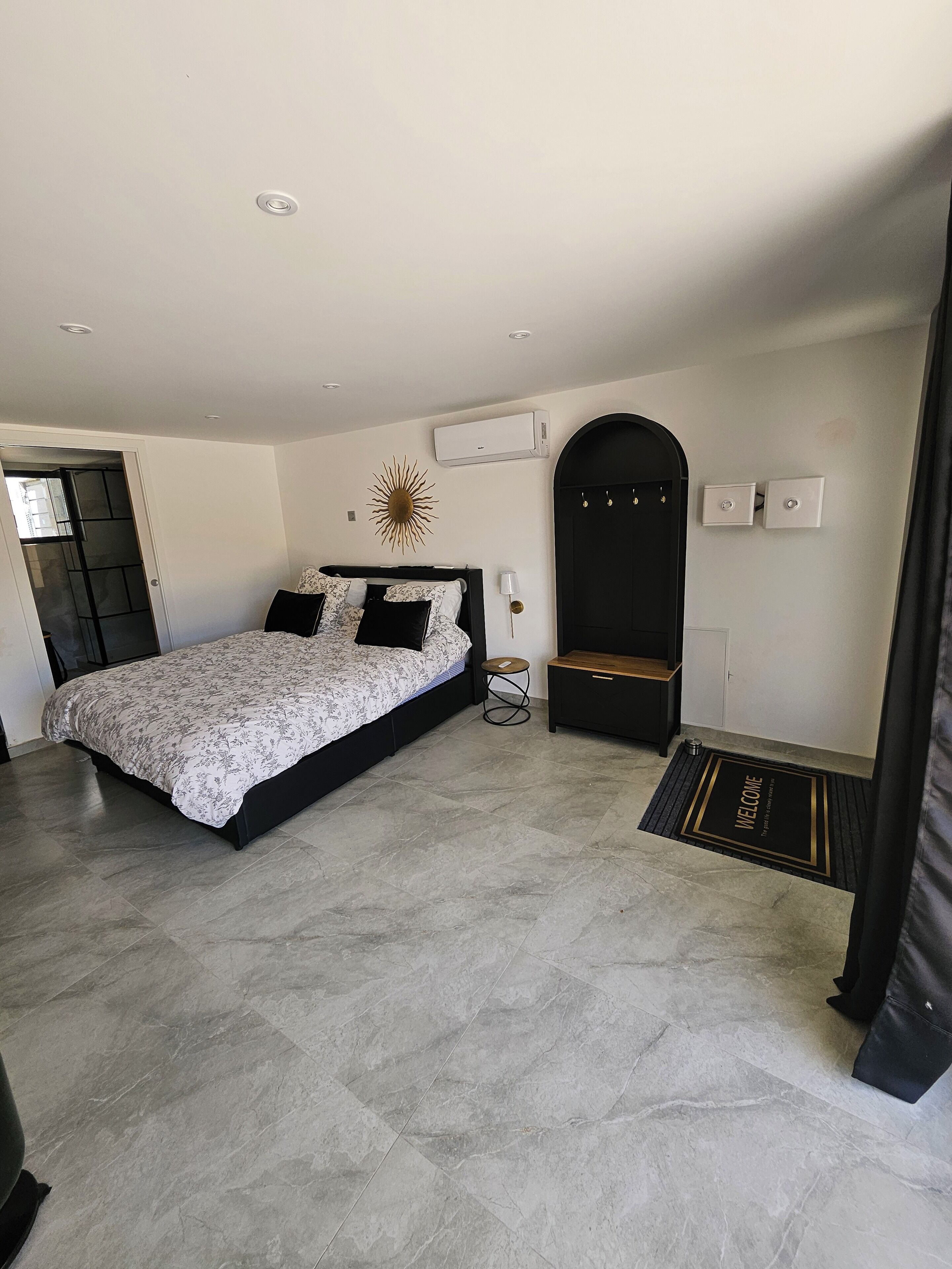 Une chambre moderne avec un grand lit, une table de chevet, un climatiseur fixé au mur et une porte avec un paillasson.