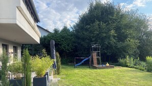 A residential backyard with a play structure, a grassy lawn, and a building with a balcony.