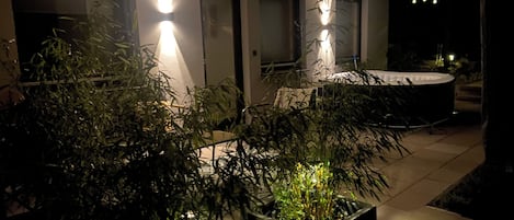 A modern outdoor area with potted plants, a hot tub, and a well-lit pathway.