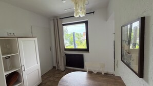 A room with a white cabinet, a round table, a window with curtains, a radiator, and a ceiling light fixture.
