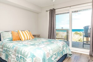 Un dormitorio con cama, almohadas, una mesita de noche y vistas al océano a través de un ventanal corredero.