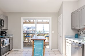 A kitchen with a view to a balcony, a dining table, and a microwave. - Dunebeg - 3BR Oceanfront Townhome; Great Views! (North Topsail Beach)