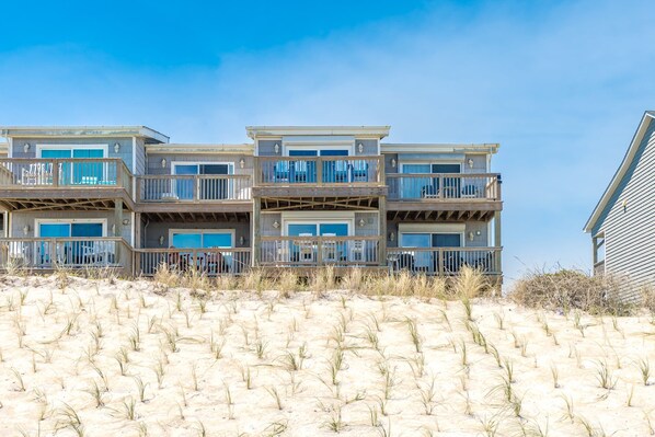 Un edificio frente a la playa con varios pisos, balcones y grandes ventanales.