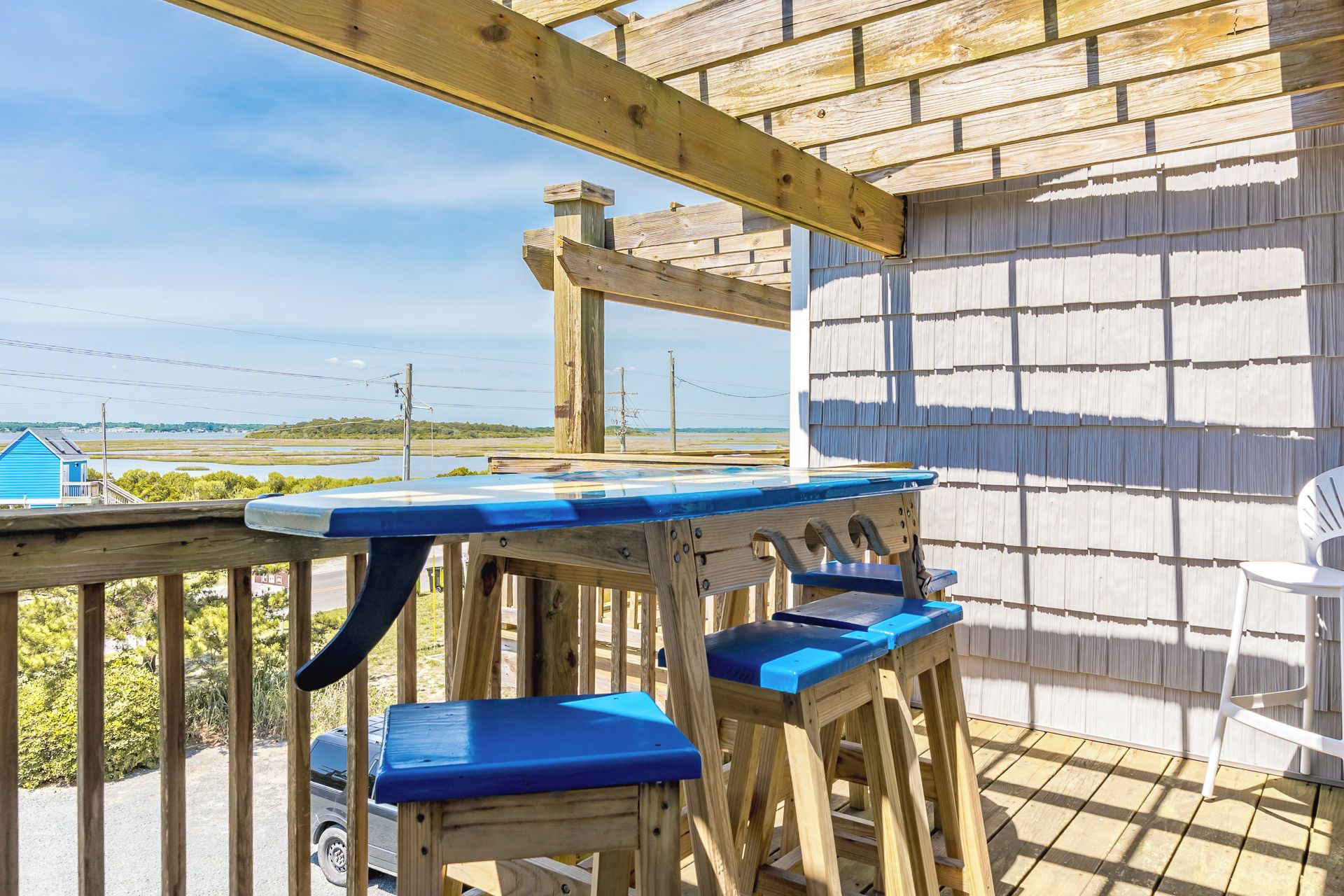 A wooden deck with a table and chairs, overlooking a landscape with a body of water and distant buildings.
