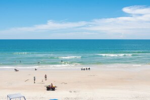 Ein Strand mit blauem Himmel, ruhiger See und Menschen, die verschiedene Aktivitäten ausüben.