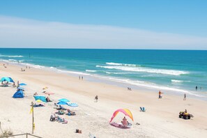 Una playa con sombrillas, sillas de baño y gente.