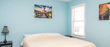 Un dormitorio con cama, mesita de noche, ventilador de techo y dos cuadros colgados en la pared.