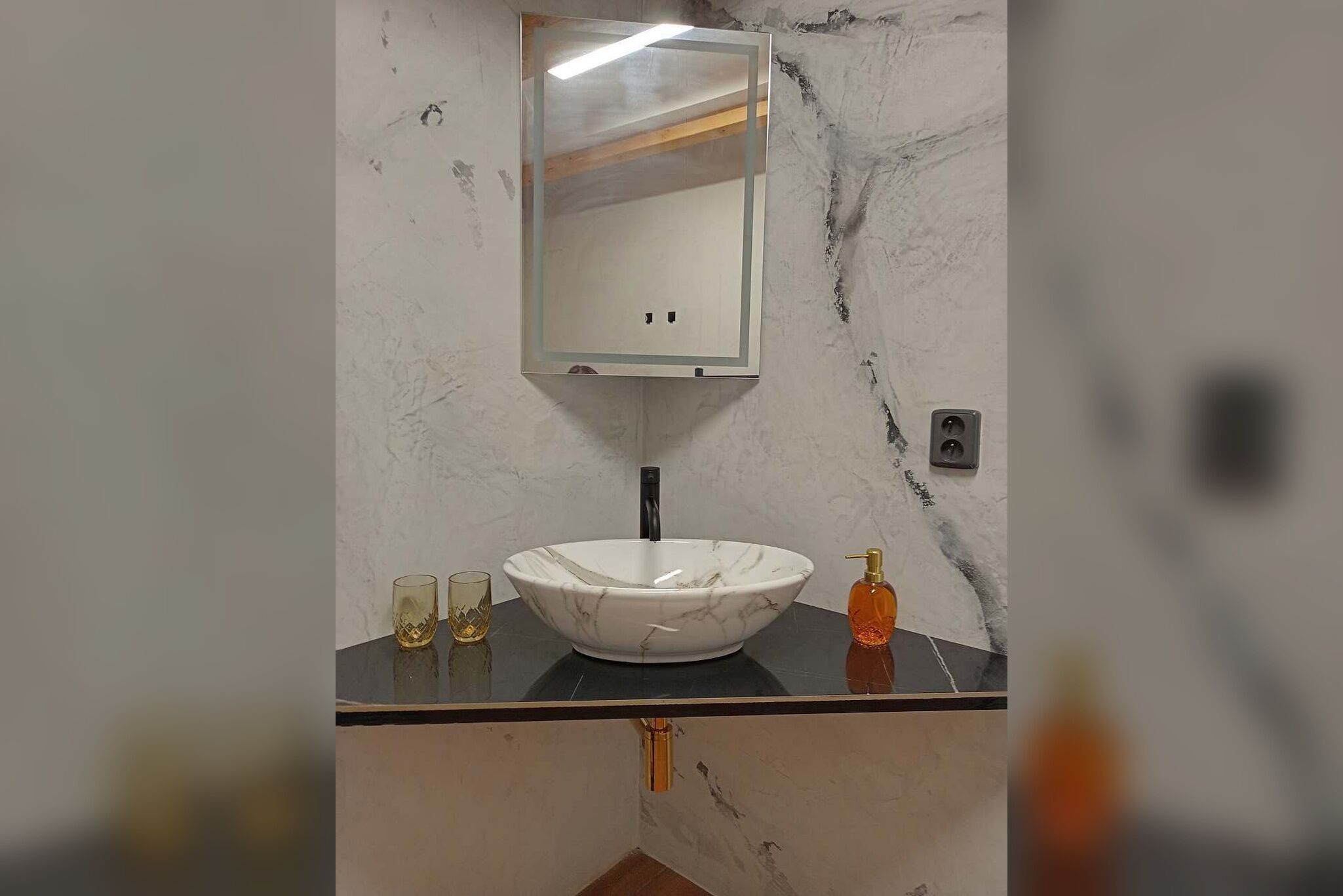 A bathroom with a marble sink, a mirror, and a soap dispenser.