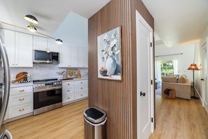 A modern kitchen with white cabinets, stainless steel appliances, and a wooden accent wall. - Newly Remodeled Waikoloa Village Retreat~Pool, Spa and Golf Views (Waikoloa Village)