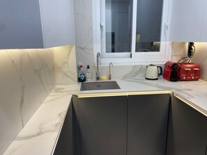 Eine moderne Küche mit Marmorarbeitsplatte, einem Spülbecken, einem Fenster und einem roten Toaster.